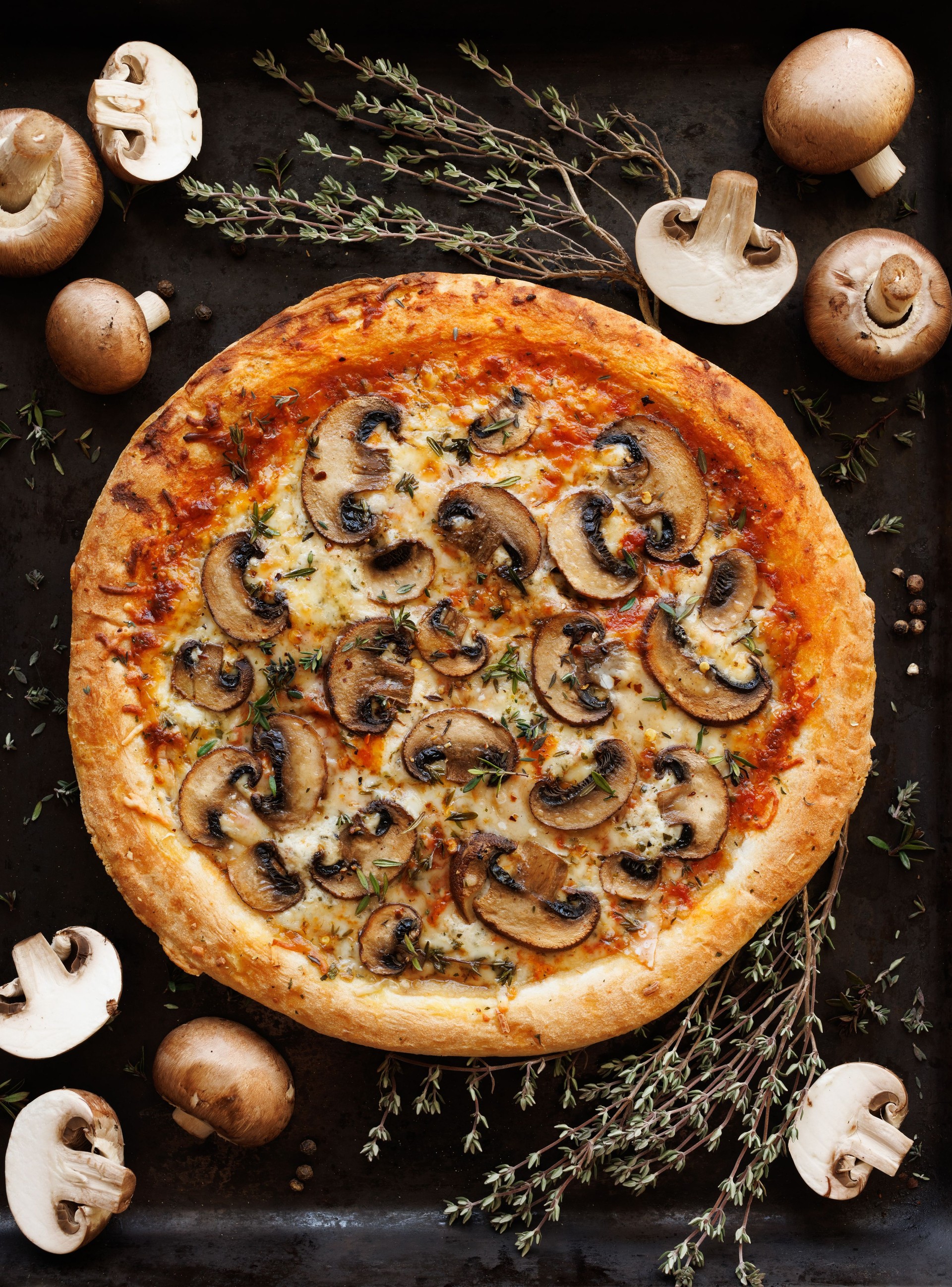 Mushroom pizza with the addition of sliced brown mushrooms, champignons and herbs on a black background