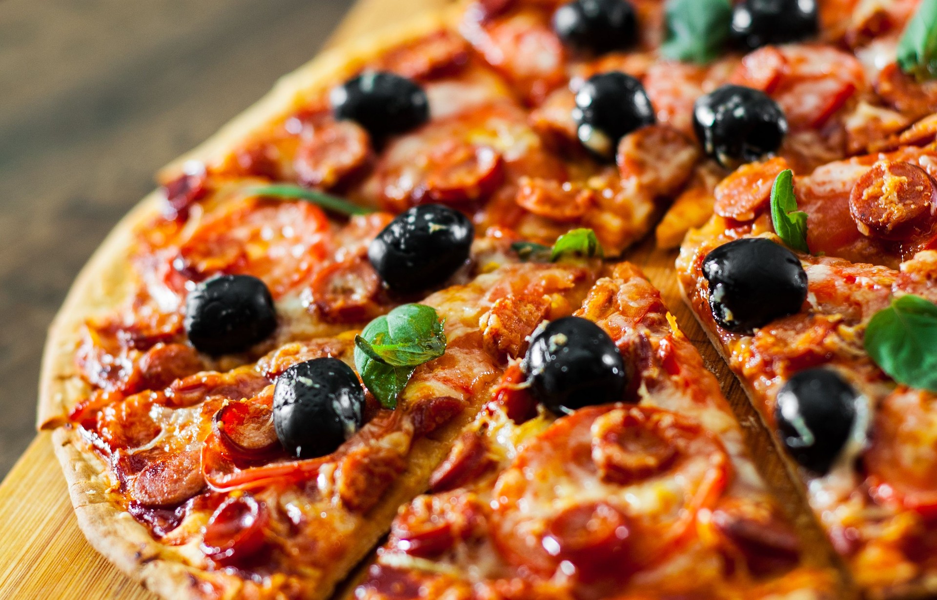 slices of Pizza with Mozzarella cheese, salami, pepper, pepperoni, Tomatoes, olives, Spices and Fresh Basil. Italian pizza on wooden background