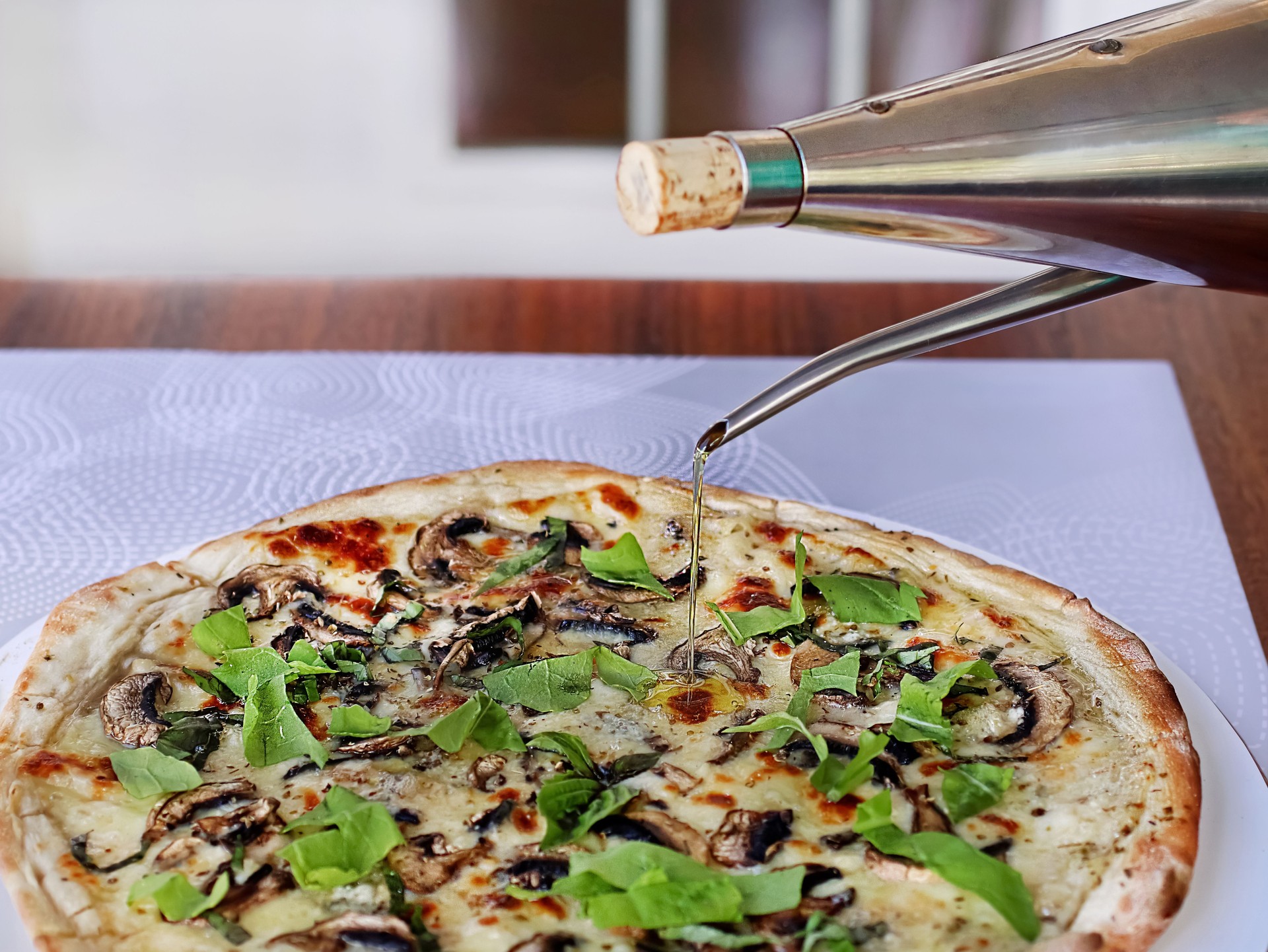 Chef pouring olive oil on delicious pizza with mushrooms and arugula